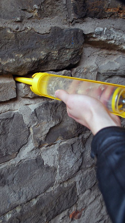 A caulking gun is being used to inject a clear gel containing fungal spores
into a crack in a wall.