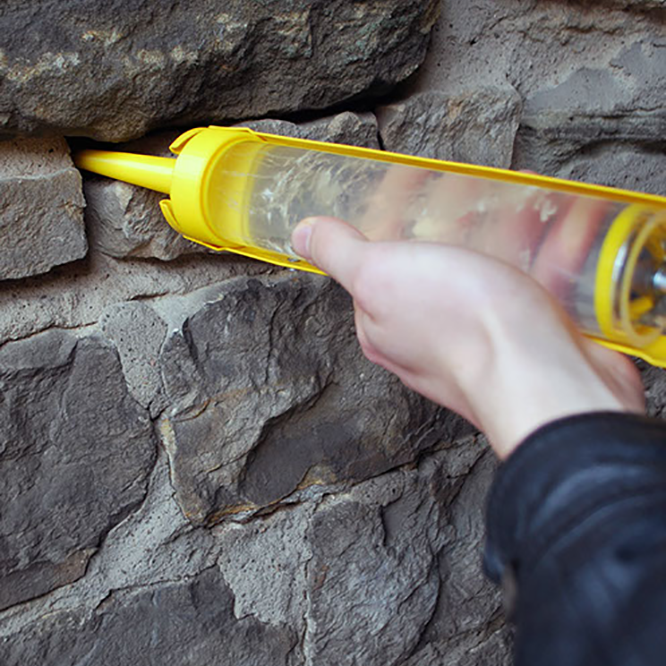 A caulking gun is being used to inject a clear gel containing fungal spores into a crack in a wall.